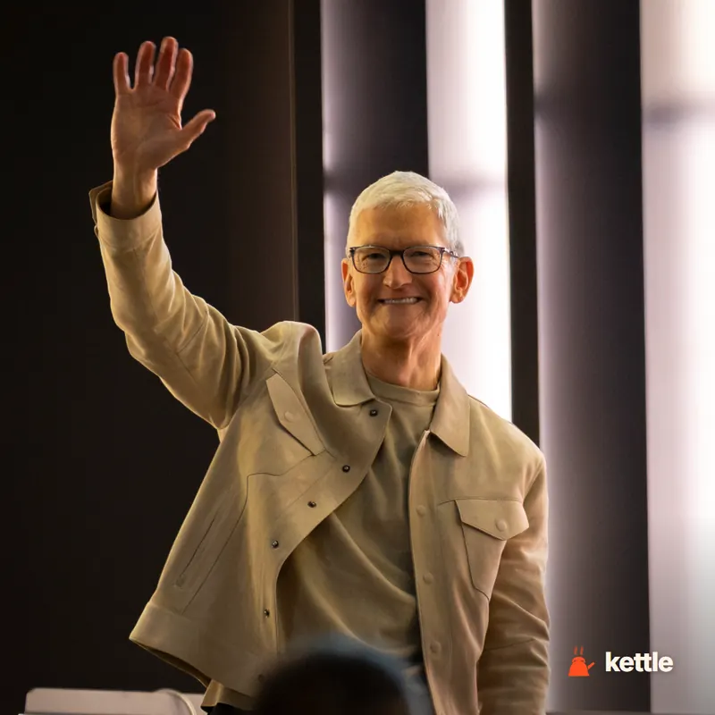 Tim Cook waving and smiling, wearing a tan jacket