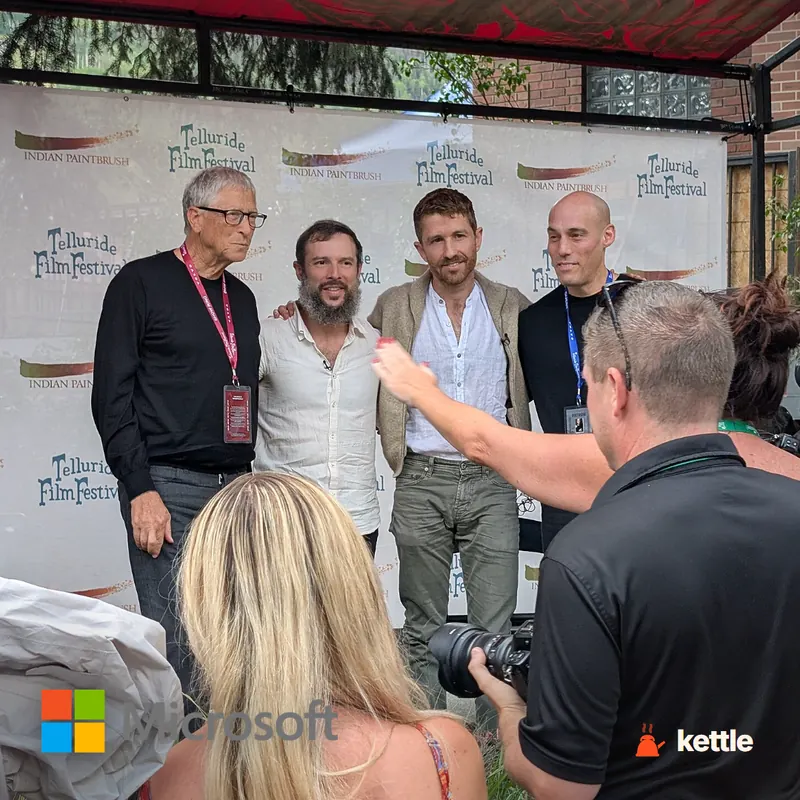Bill Gates posing with three other men at the Telluride Film Festival step-and-repeat, with a Microsoft logo overlay in the corner