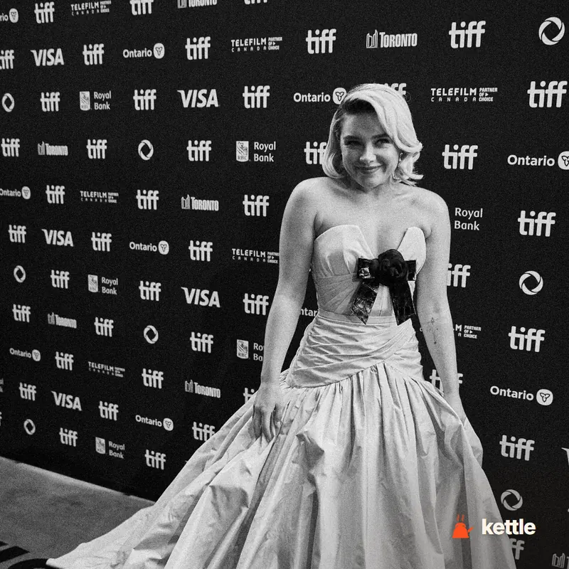 A woman in a strapless white gown with a black bow detail posing at a TIFF red carpet step-and-repeat, likely Florence Pugh