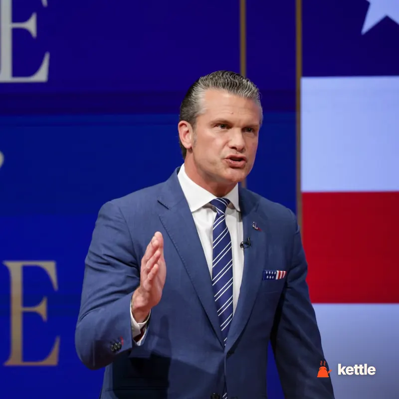 Pete Hegseth speaking on stage, gesturing, with American flag backdrop