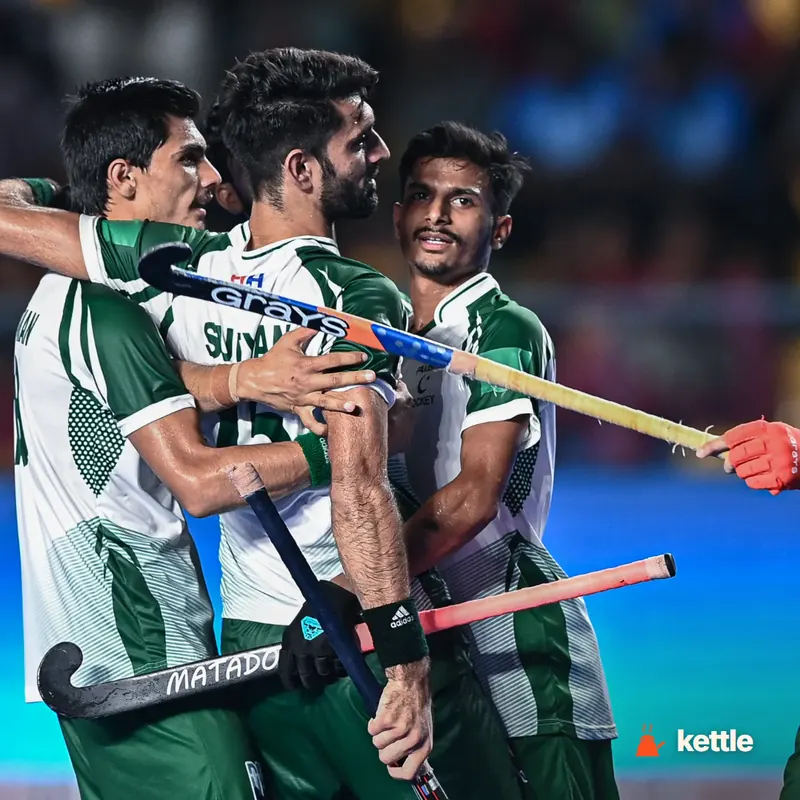 Pakistan field hockey players in green/white kits celebrating together on the pitch, holding sticks