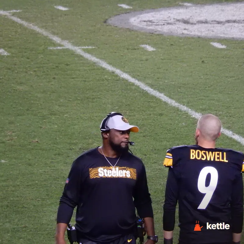 Mike Tomlin wearing a Steelers shirt and headset on the sideline, next to a player named Boswell