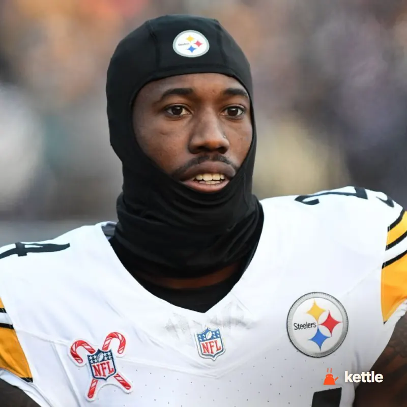 A football player in a white Steelers jersey wearing a black hooded balaclava, close-up portrait with Steelers and NFL patches visible